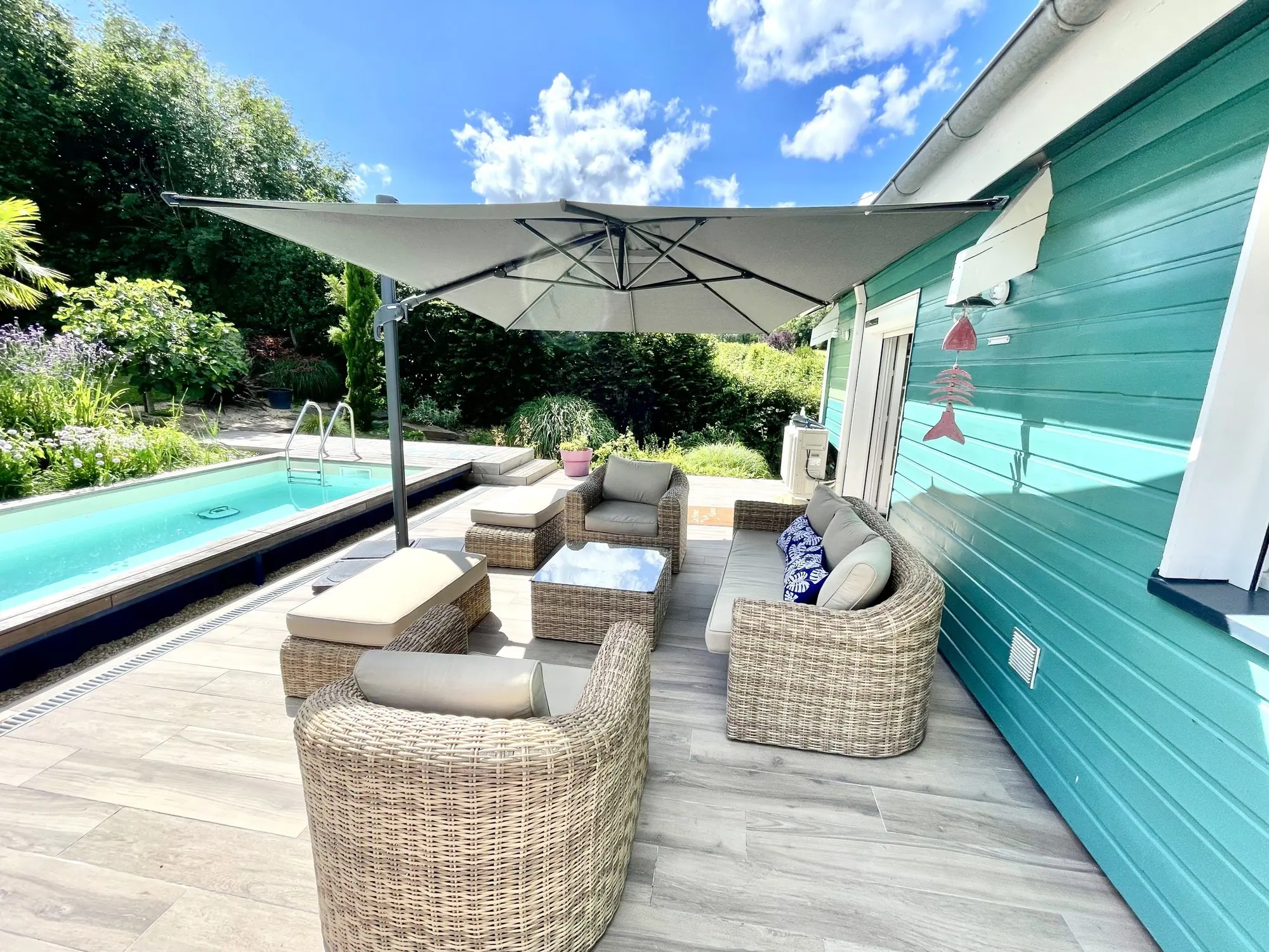 La terrasse, le salon de jardin sous le parasol, la piscine le long du chalet
