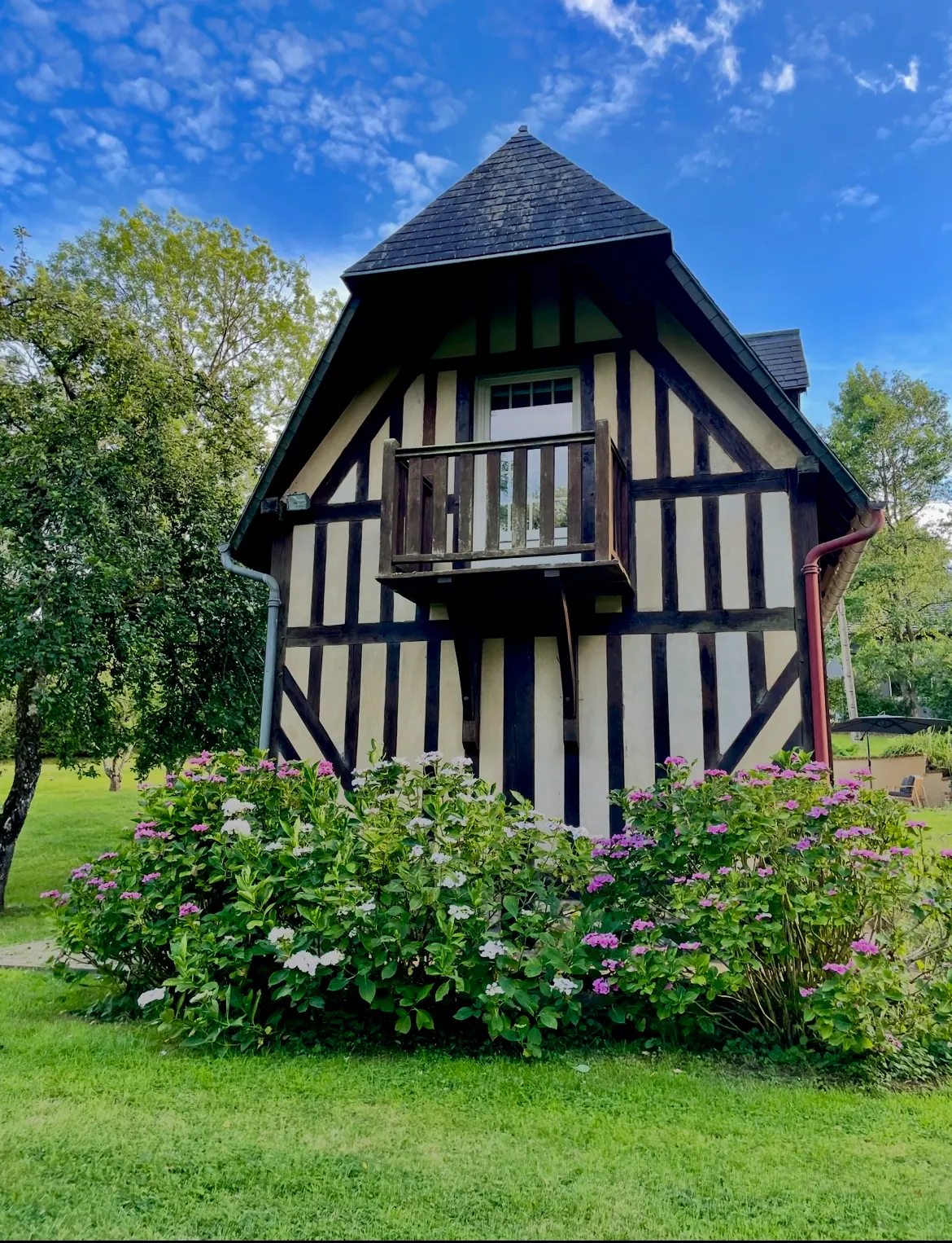La façade à colombages de Reinette Grise, son balcon de bois au-dessus des hortensias