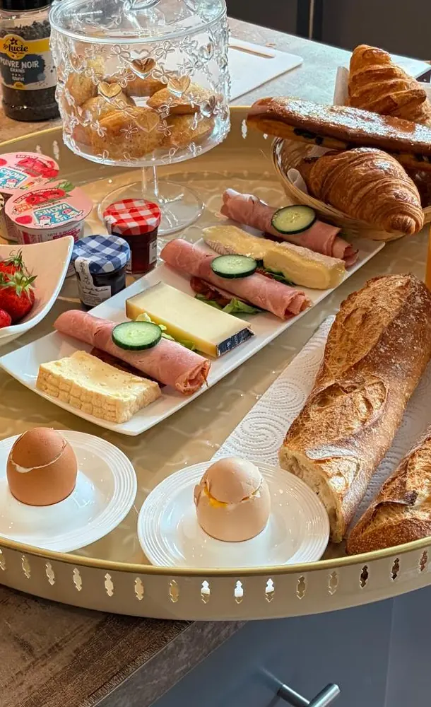 Le plateau du brunch sur l’îlot de la cuisine : œufs à la coque, fraises, fromage et jambon, baguettes et croissants