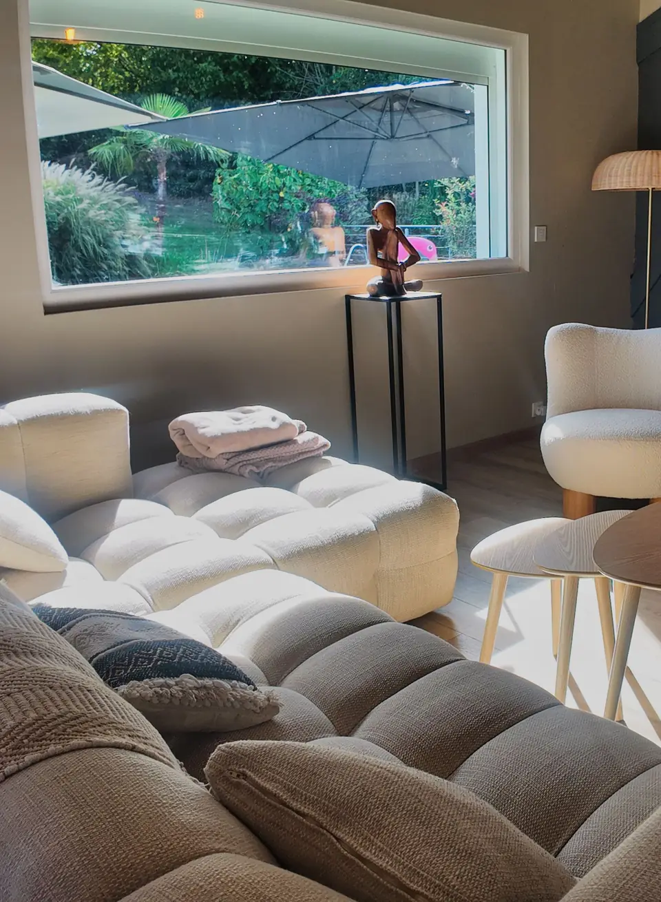 Le salon du Chalet Normand : le grand canapé clair, un fauteuil et la baie qui donne sur la piscine