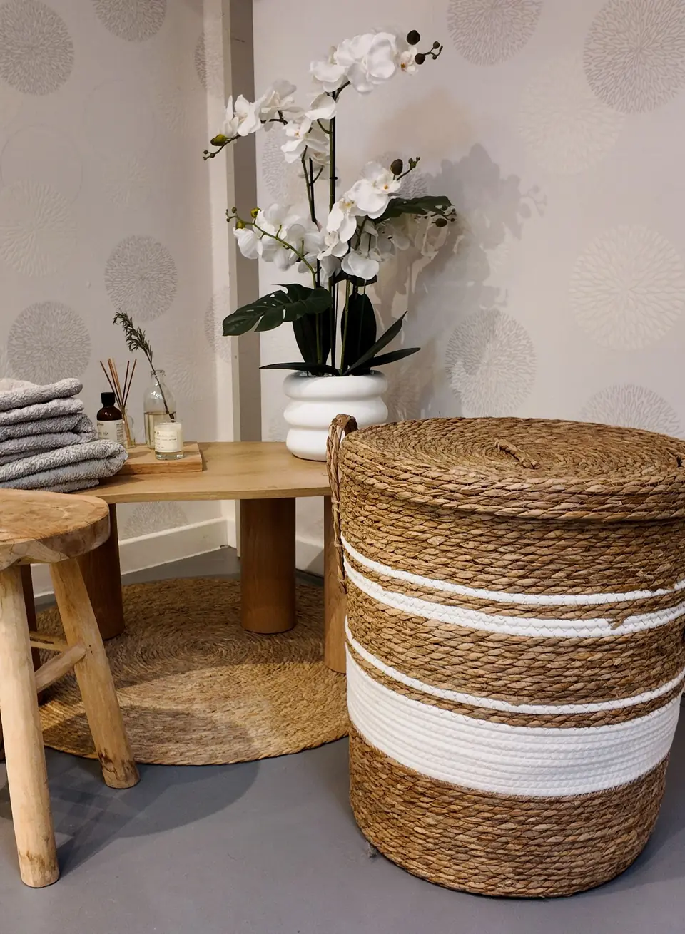 Des serviettes pliées, un tabouret de bois brut, une orchidée blanche et un panier en osier